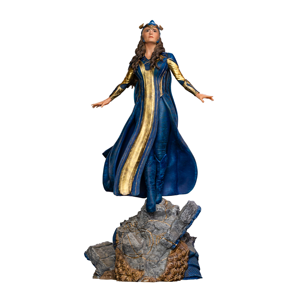 Una donna in un vestito blu e oro è in piedi su una roccia. Ha le braccia aperte. Lo sfondo è bianco.