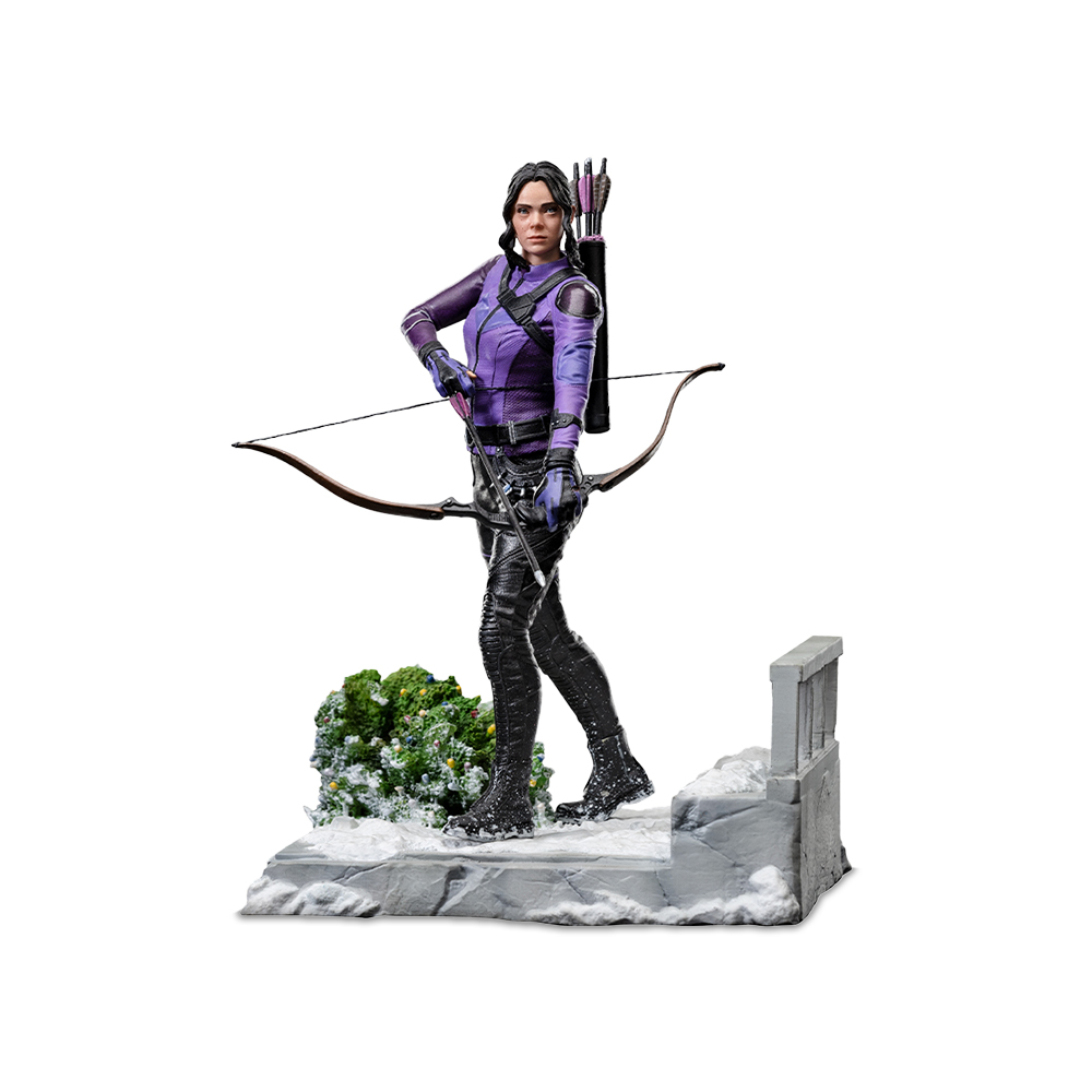 Statua di una donna in abito viola e nero con arco. In piedi su una piattaforma innevata. Sfondo bianco.