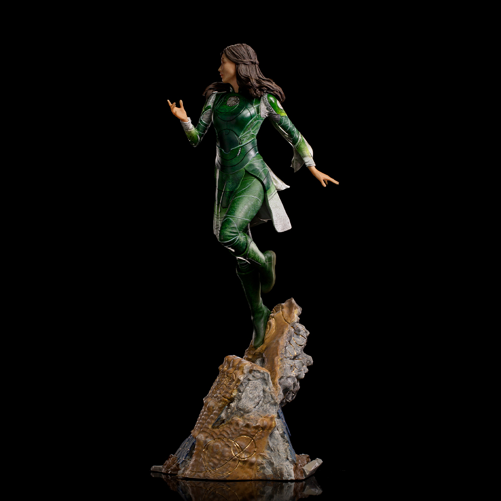 Una statua di una donna in costume verde. È a mezz'aria, in piedi su una base di roccia, su sfondo nero.