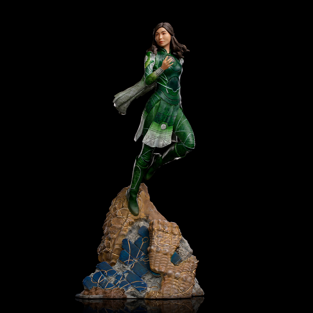 Statua di una donna in costume verde, a metà salto su una roccia. Lo sfondo è nero. La statua ha i capelli castani e indossa un mantello.