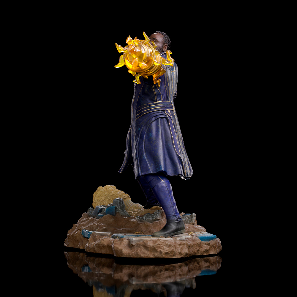 Una statua di un uomo in abito blu che tiene in mano un oggetto giallo brillante. Si trova su una base rocciosa su sfondo nero.