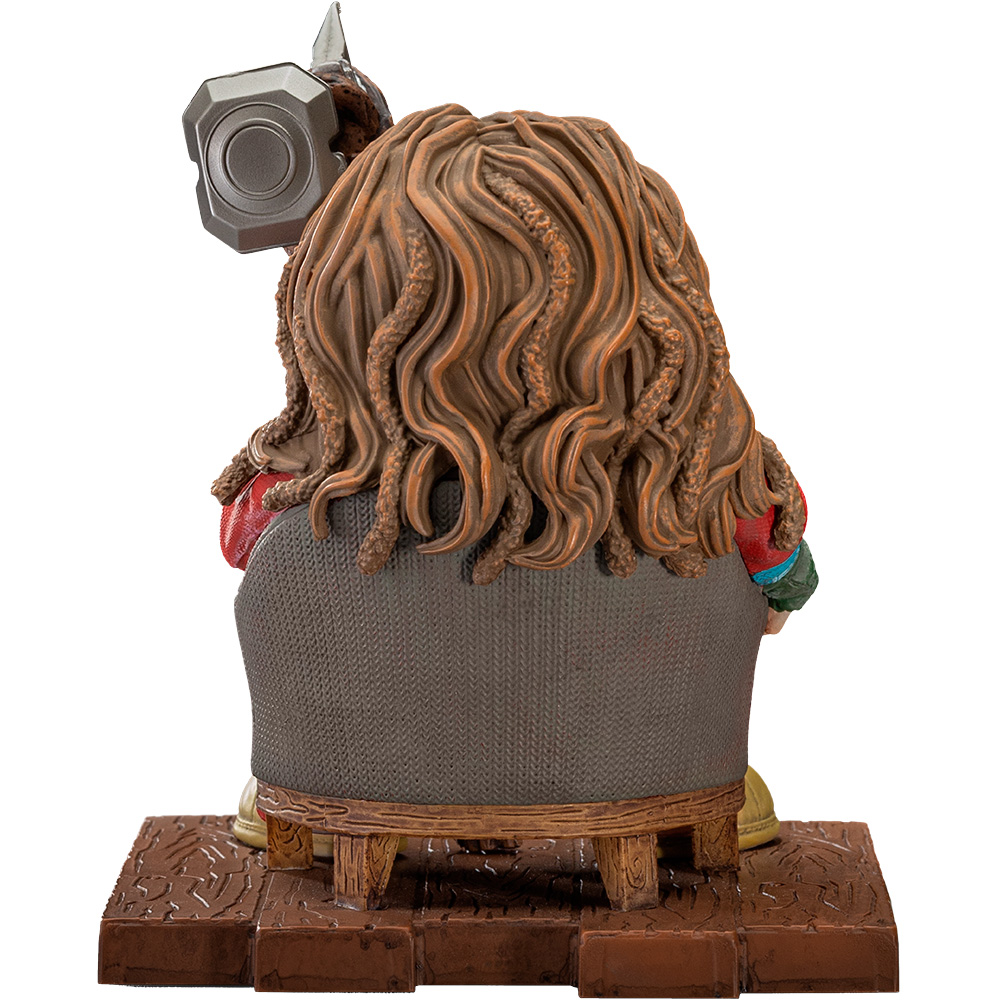 Statua di una persona con lunghi capelli castani, seduta, con un martello. La sedia è marrone e la base è una piattaforma marrone.