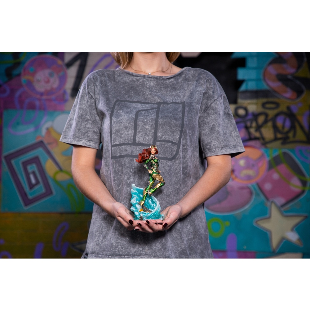 Una persona tiene in mano una statuina di Aquaman. La statuina è dettagliata e la persona indossa una maglietta grigia. Lo sfondo ha graffiti.