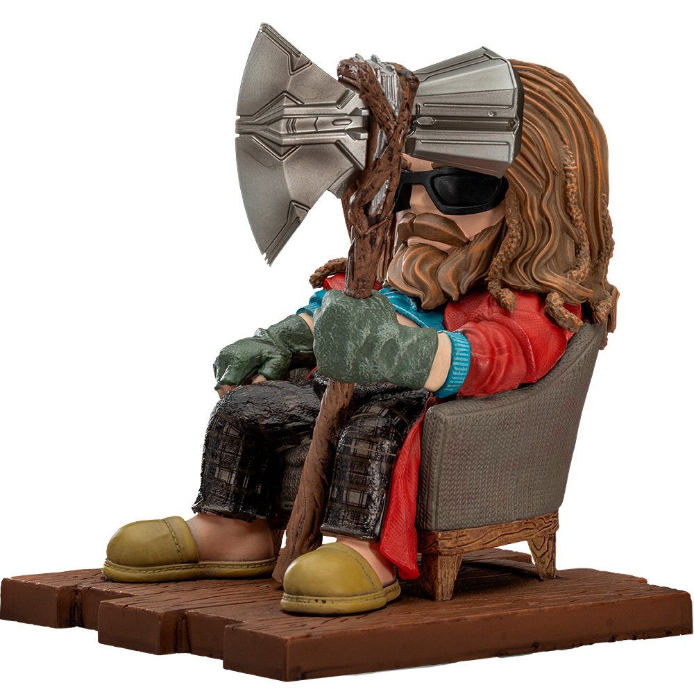 Una figura di Thor con occhiali da sole, che tiene un'ascia, seduto su una sedia, con una giacca rossa, guanti e pantofole gialle.