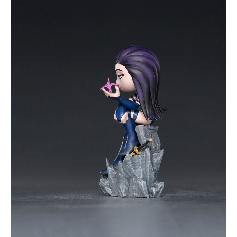 Una statuina di una donna con i capelli viola, che indossa un vestito blu, seduta su una pietra. Tiene in mano un oggetto rosa. È presente una spada.