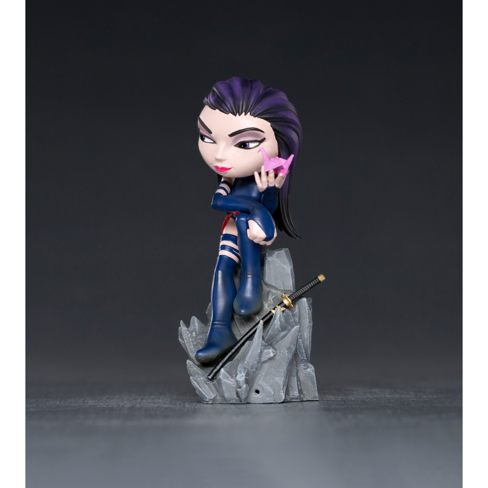 Statuina di Psylocke con capelli viola, che tiene un origami rosa. È seduta su una roccia, con una katana nelle vicinanze. Sfondo scuro.
