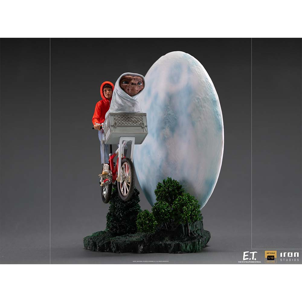 Una statua di E.T. ed Elliott in bicicletta, che volano davanti a una grande luna. Ci sono cespugli verdi in basso.