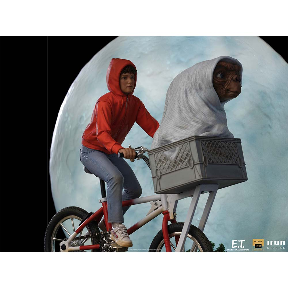 Un ragazzo con la felpa rossa va in bicicletta con E.T. in un cestino. Lo sfondo presenta una grande luna.
