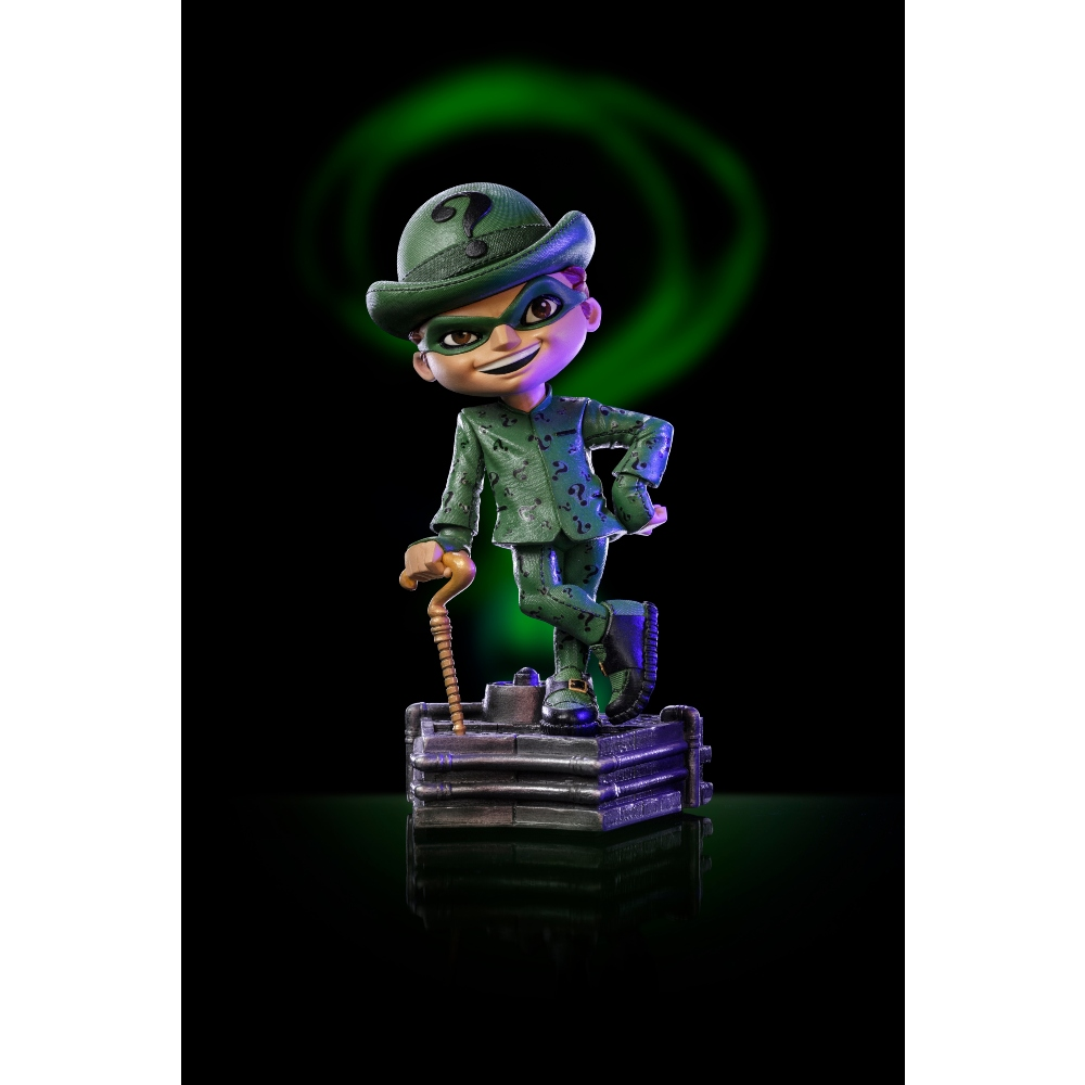 Un personaggio dei cartoni animati di Enigmista è in piedi su una base di metallo, indossa un abito, un cappello e una maschera verdi. Una spirale verde è dietro di lui, su sfondo nero.