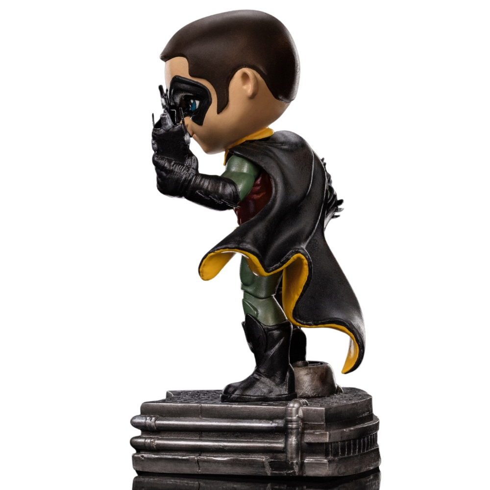 Una statuetta di Robin è in piedi su una base. Indossa un mantello nero con fodera gialla, una maschera nera e un costume verde e rosso.
