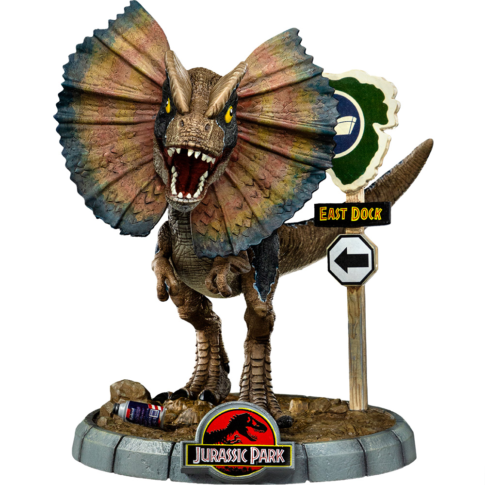Una statua di dinosauro Dilophosaurus con un'ampia gola, bocca aperta e occhi gialli, si trova vicino a un cartello 'East Dock' con il logo di Jurassic Park.