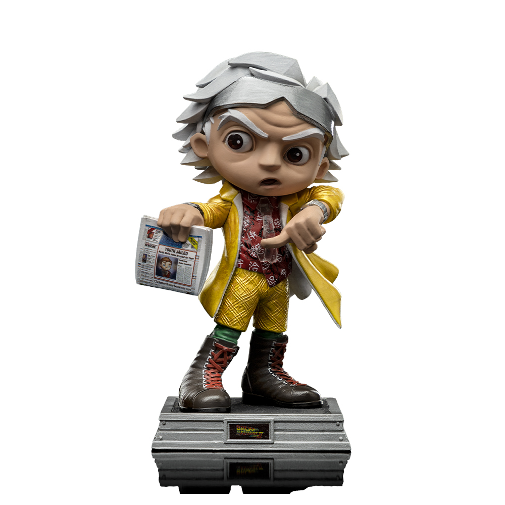 Statuetta di Doc Brown che indica. Indossa un cappotto giallo, una camicia fantasia e pantaloni. Tiene in mano un giornale. La base dice "Ritorno al futuro".