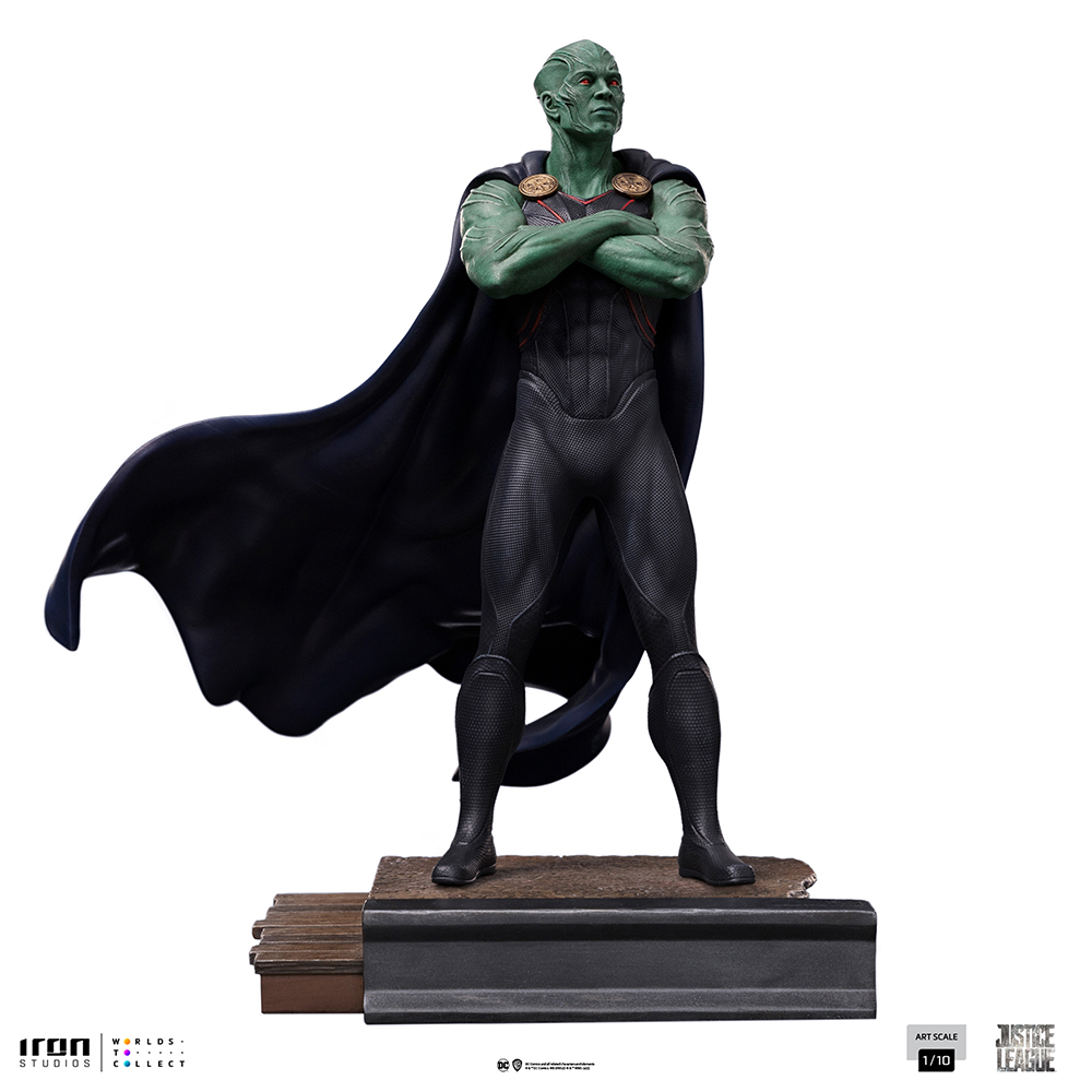 Una statua di Martian Manhunter con pelle verde, tuta nera e mantello. In piedi su una base, con le braccia conserte e lo sguardo in avanti.