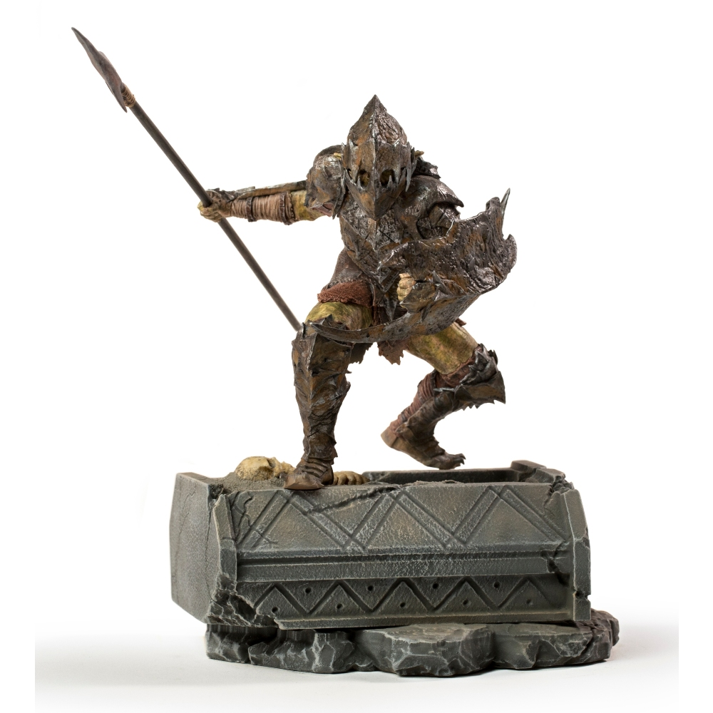 Statua di guerriero orco con lancia e scudo. Si trova su una base di pietra. L'orco indossa un'armatura marrone e ha una posa minacciosa.