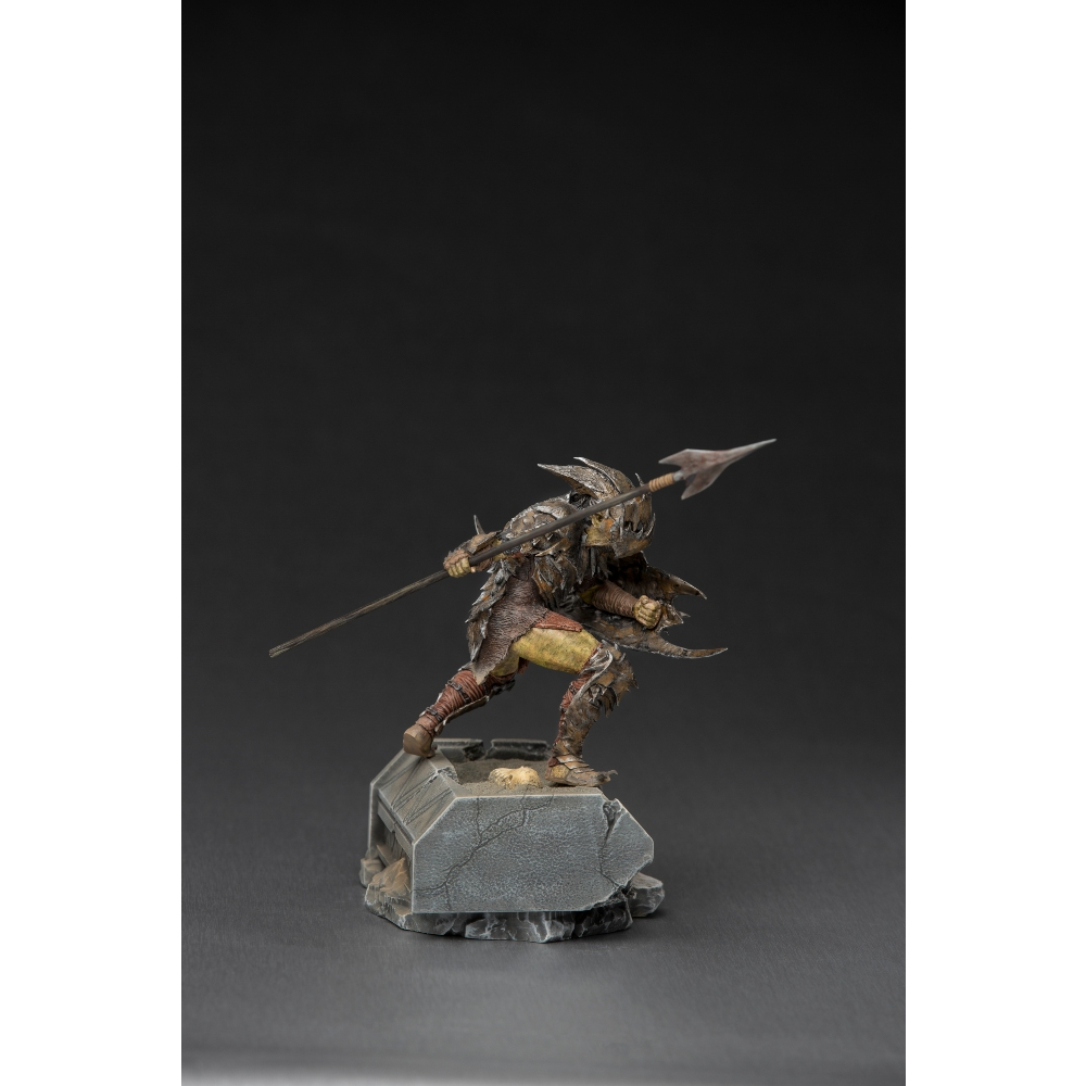 Una statuetta di un guerriero orco con una lancia su una base di pietra. L'orco indossa un'armatura e tiene una lancia, su sfondo nero.