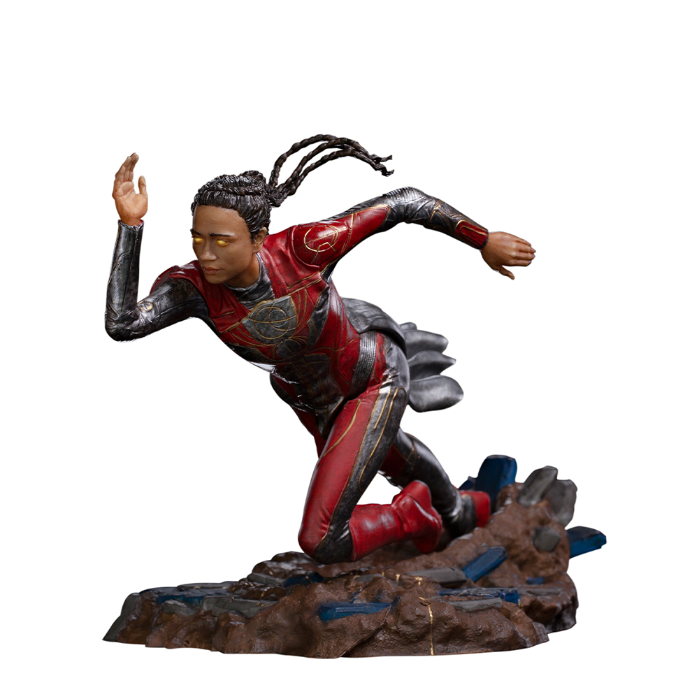 Una statua di una donna in tuta rossa e nera, corre su una base rocciosa con il braccio destro alzato. I suoi occhi brillano.
