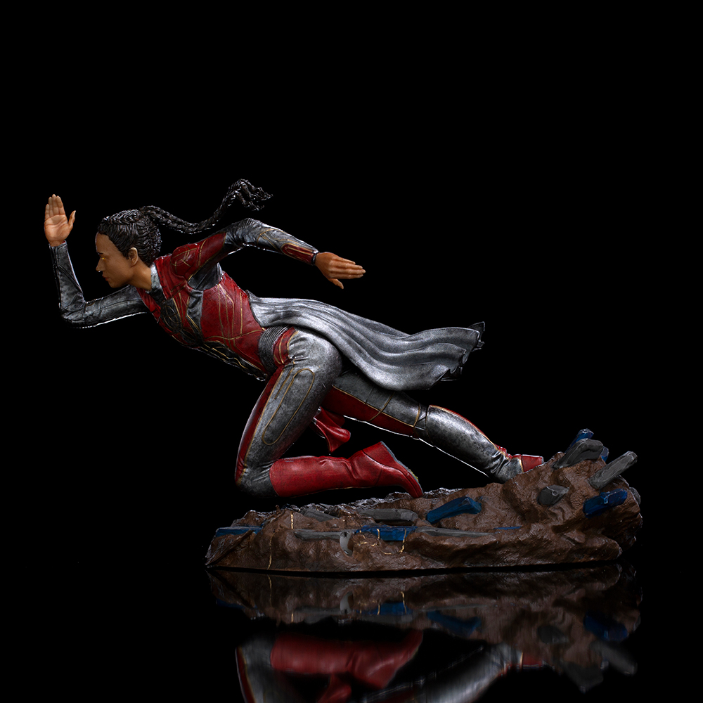 Una statuetta di una donna in abito rosso e argento che corre. È su una base marrone con accenti blu. Sfondo nero.