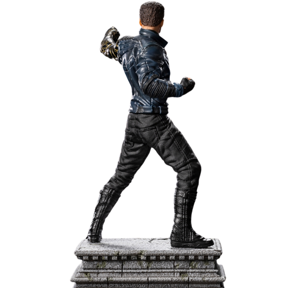 Una statuetta di un uomo con giacca e pantaloni di pelle, che colpisce. Si trova su una piattaforma di pietra. Lo sfondo è bianco.