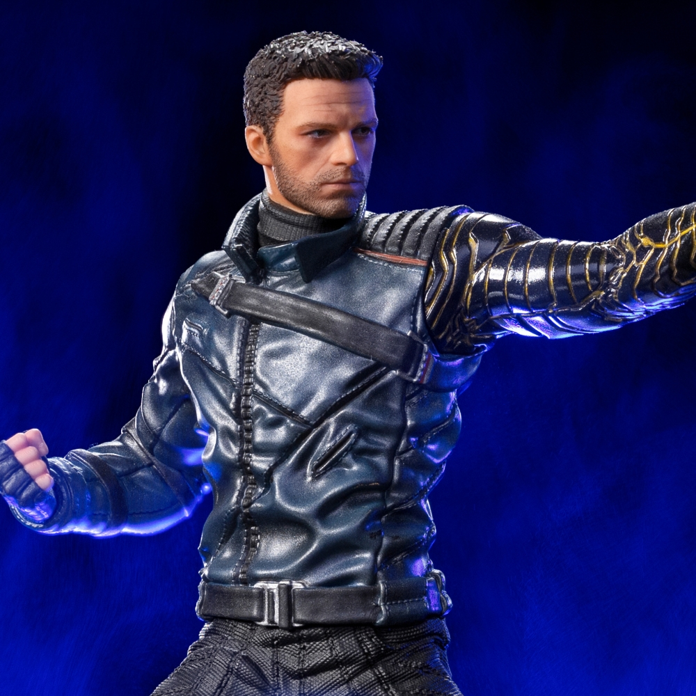 Figura di un uomo con giacca blu e braccio metallico, rivolto a destra. Capelli scuri ed espressione seria. Sfondo blu.