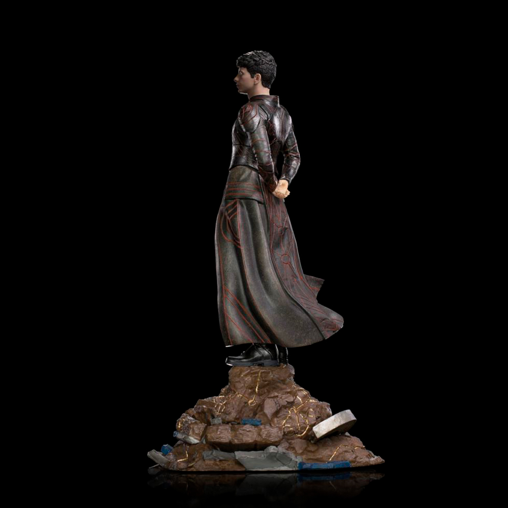 Una statua di una persona in costume scuro è in piedi su una base rocciosa su sfondo nero. La figura ha i capelli corti e scuri.