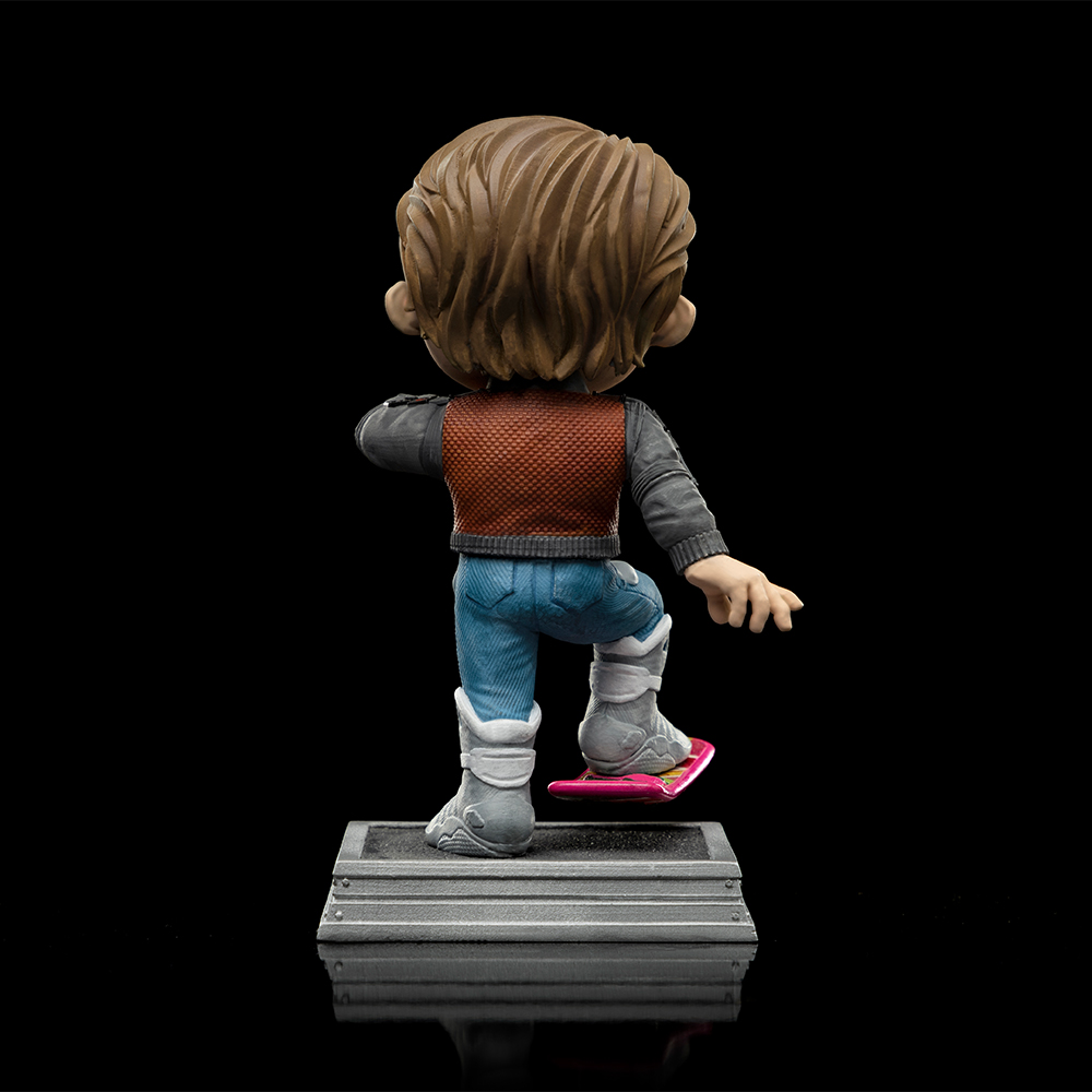 Statuetta di un uomo su un hoverboard rosa, con gilet marrone, jeans blu e stivali grigi. Vista posteriore su sfondo nero.