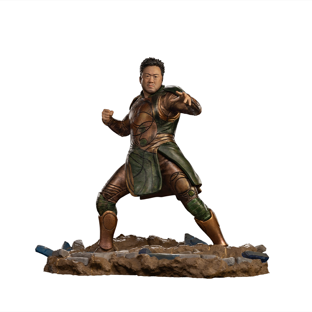 Figura di un uomo in armatura ornata, in posa di arti marziali, su una base rocciosa. Ha capelli scuri e un'espressione concentrata.
