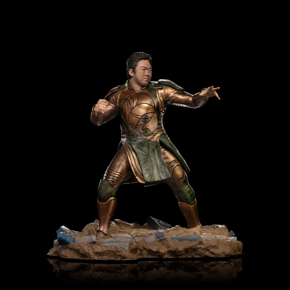 Una statuina di un uomo in abito dorato e verde, in posa da combattimento. Si erge su una base rocciosa su sfondo nero.