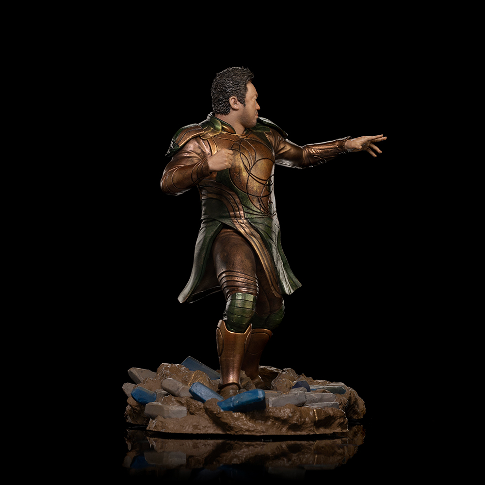 Statua di un uomo in armatura bronzo e verde. Indica in avanti, in piedi su una base di macerie, su sfondo nero.