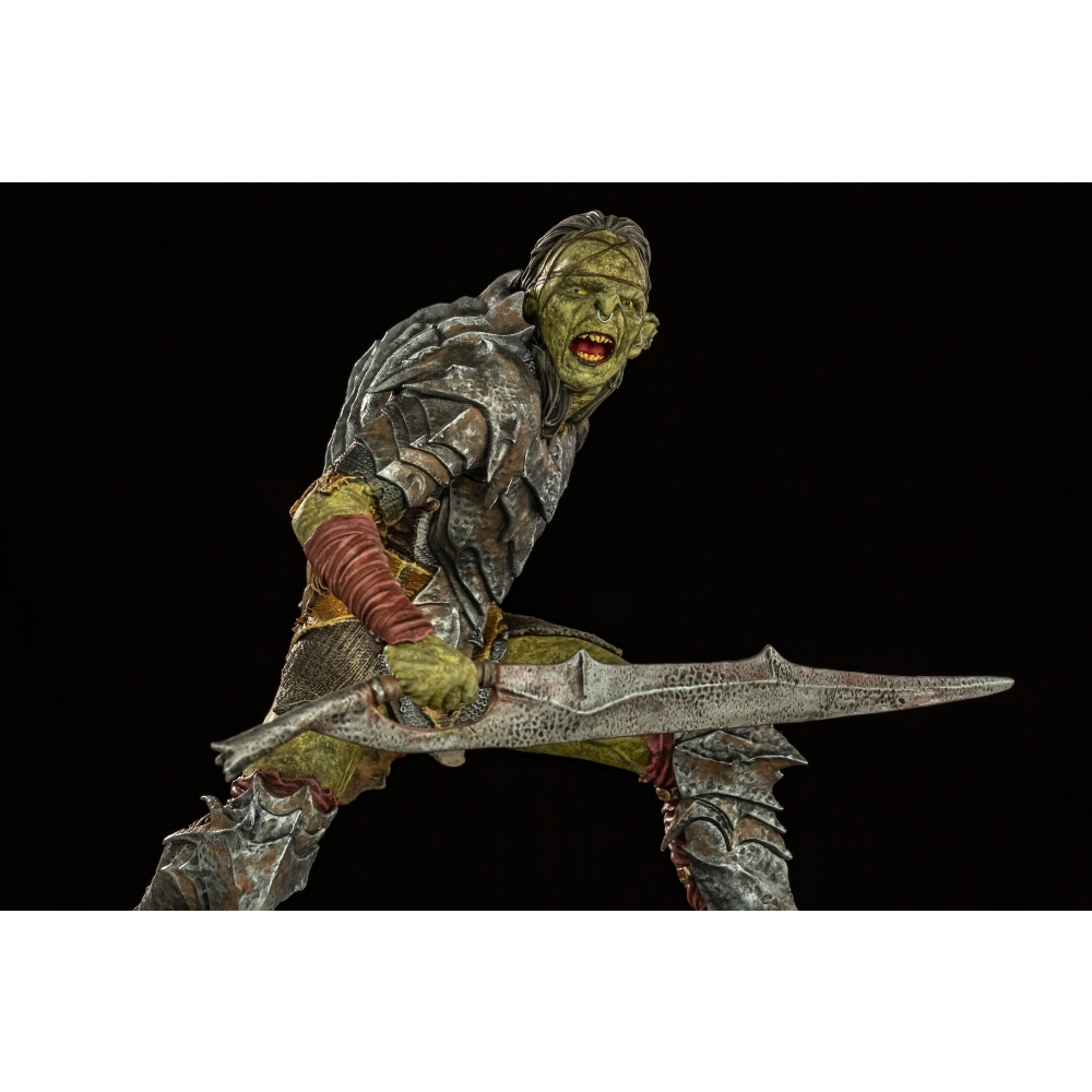 Una statuetta di orco con una spada. Ha la pelle verde, l'armatura e la bocca aperta. Lo sfondo è nero.