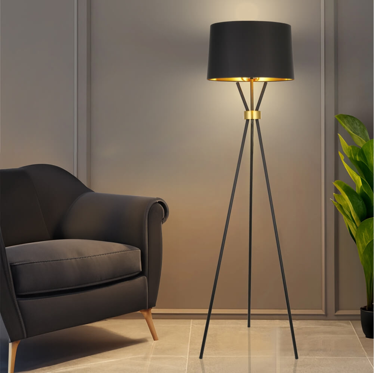 Eine schwarze Lampe mit goldenem Innenraum steht in einem Raum. Links ein schwarzer Sessel und rechts eine Pflanze.