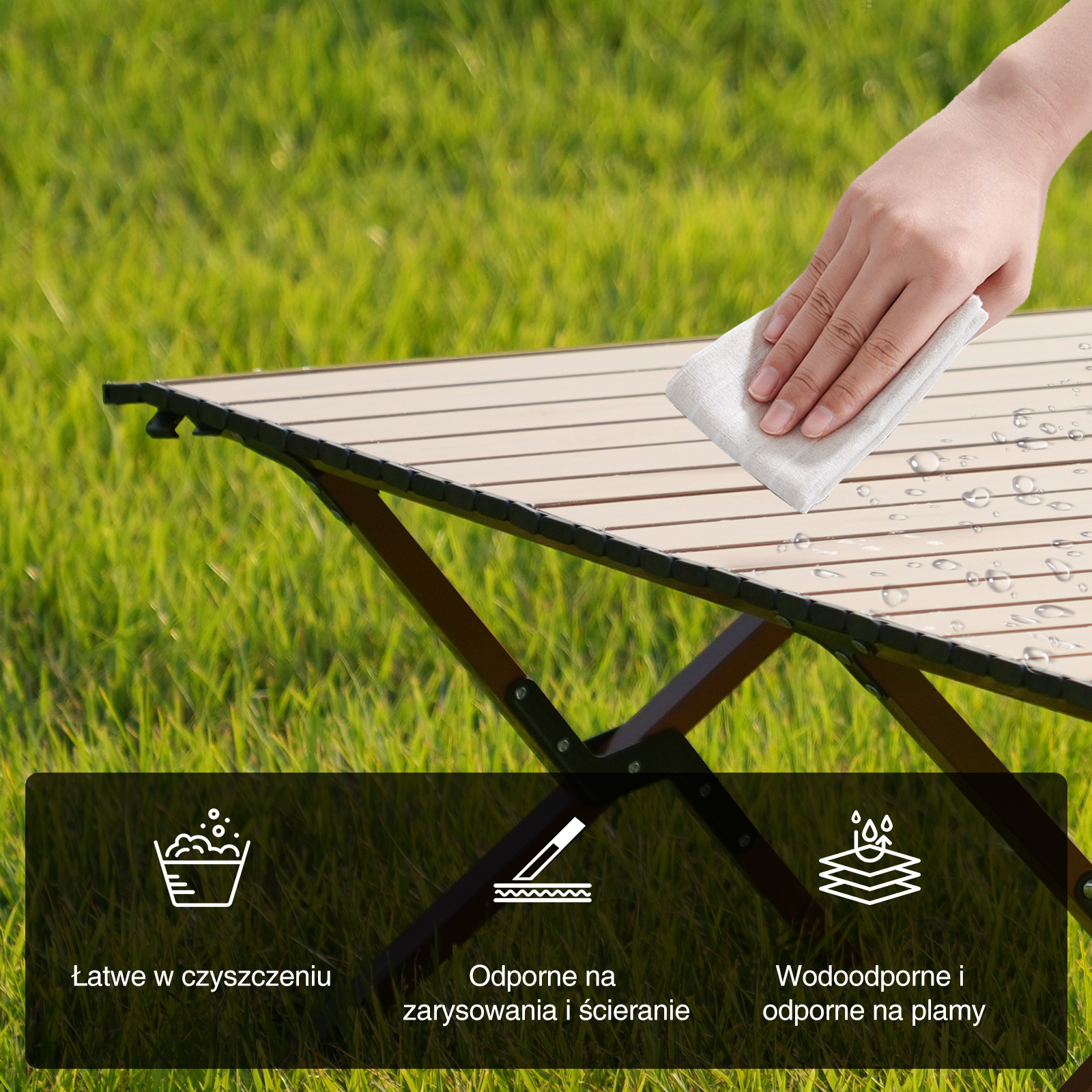 Osoba czyści beżowy drewniany stół białą szmatką, widoczne krople wody. Tło to zielona trawa.