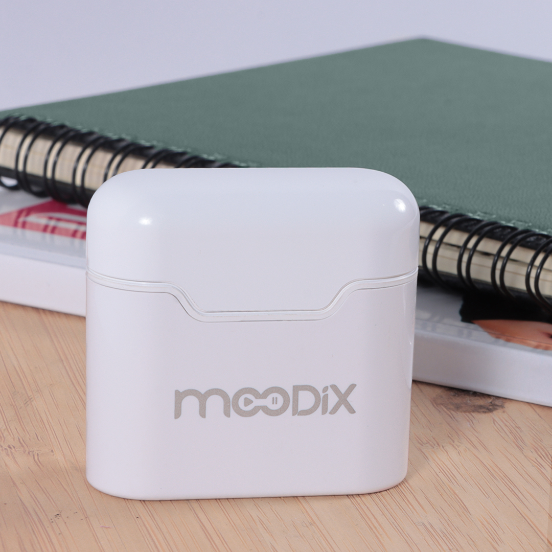 'mooDIX' yazılı beyaz bir kulaklık kutusu, ahşap bir yüzeyde bir not defterinin yanında duruyor.