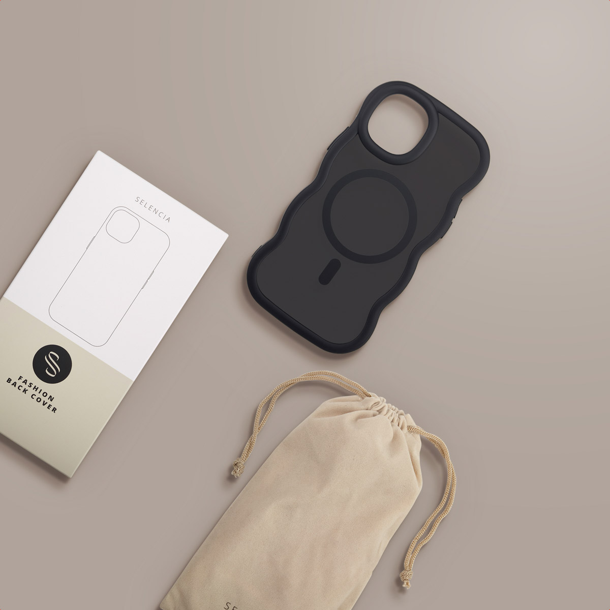 Une coque de téléphone noire avec un cercle magnétique, une boîte blanche et un sac beige sur une surface brun clair.