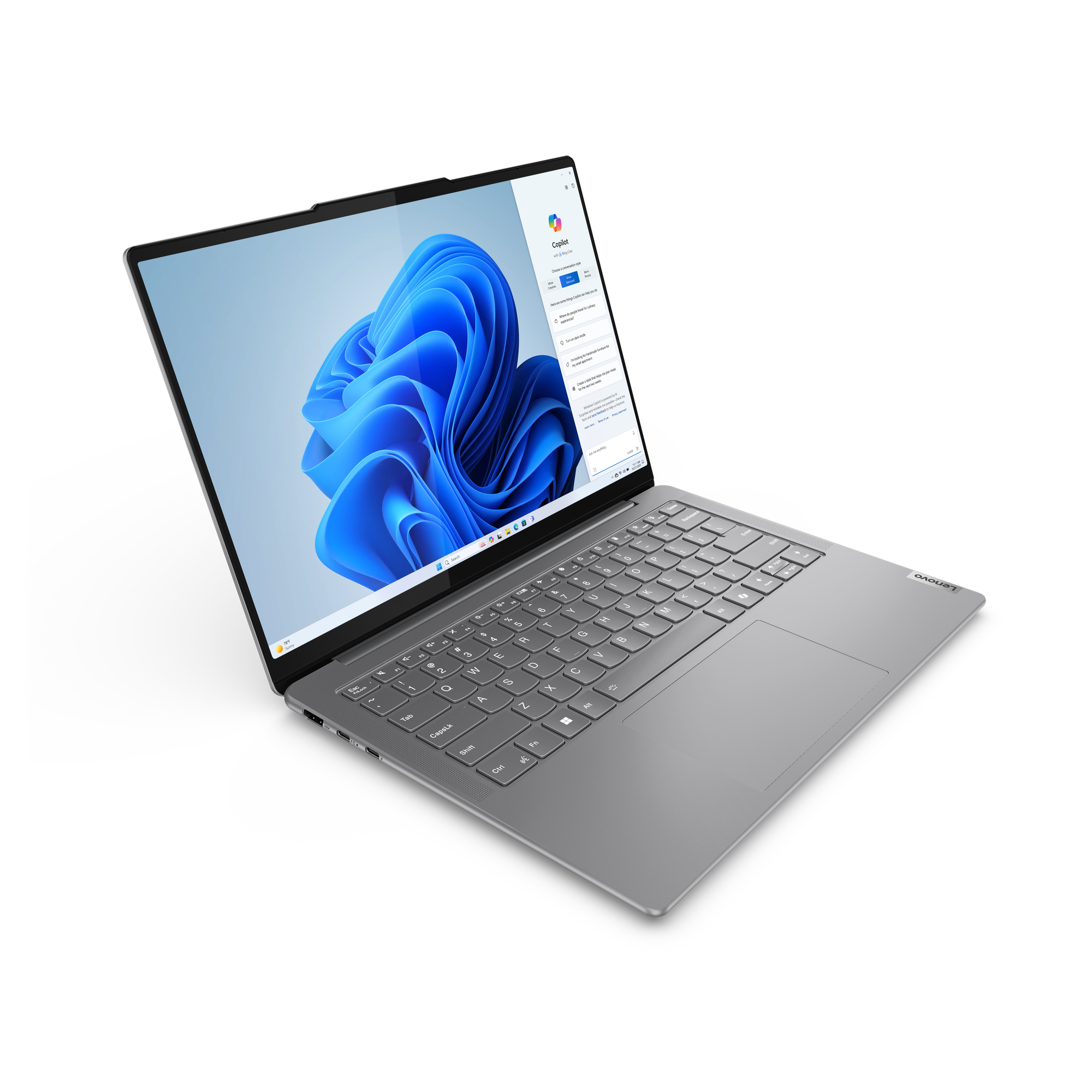 Un laptop Lenovo argentato mostra uno sfondo blu di Windows. Lo schermo mostra un'interfaccia Copilot, con tastiera visibile.