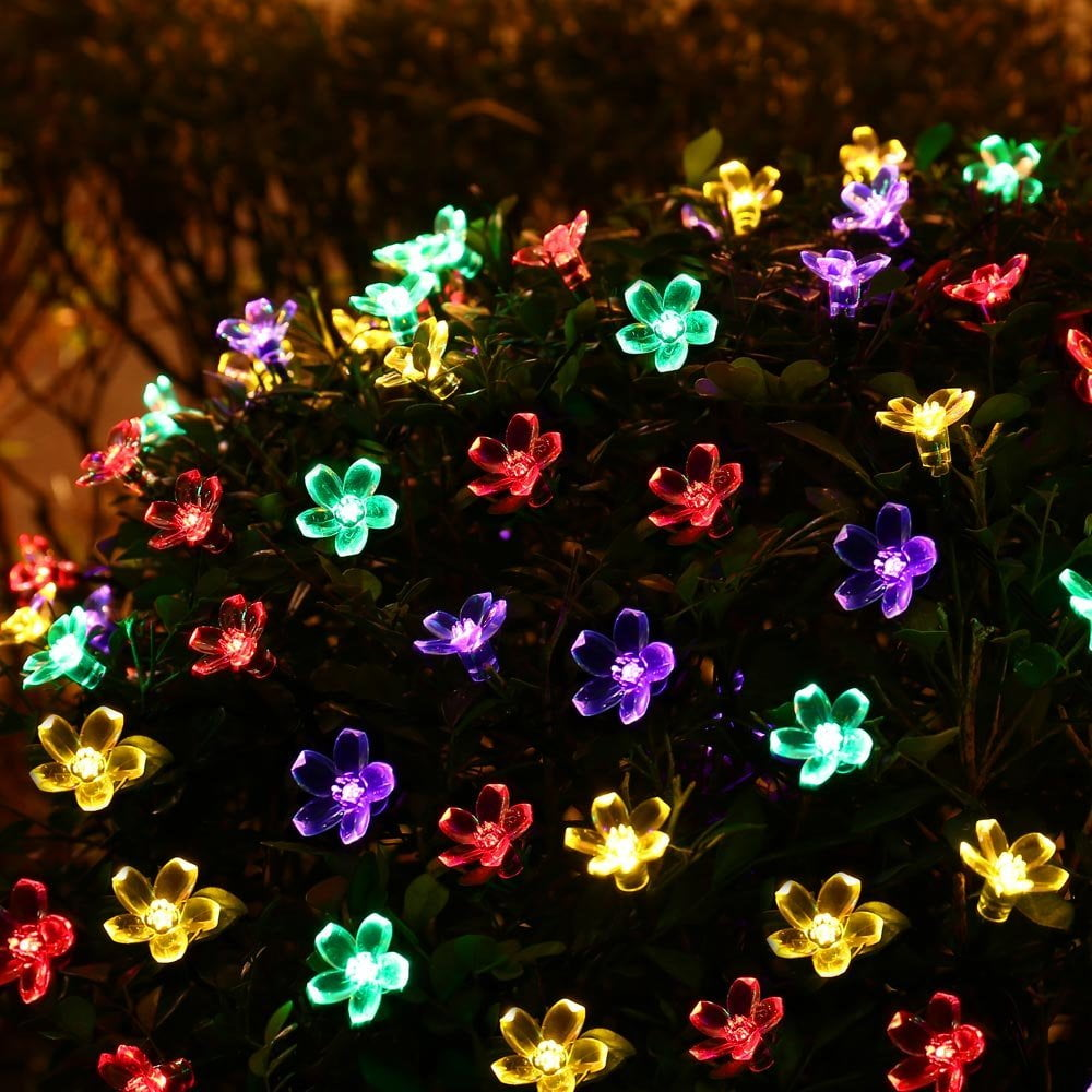 Nahaufnahme von leuchtenden, bunten blütenförmigen Lichtern auf einem grünen Busch. Die Lichter haben verschiedene Farben wie Rot, Grün, Gelb und Lila.