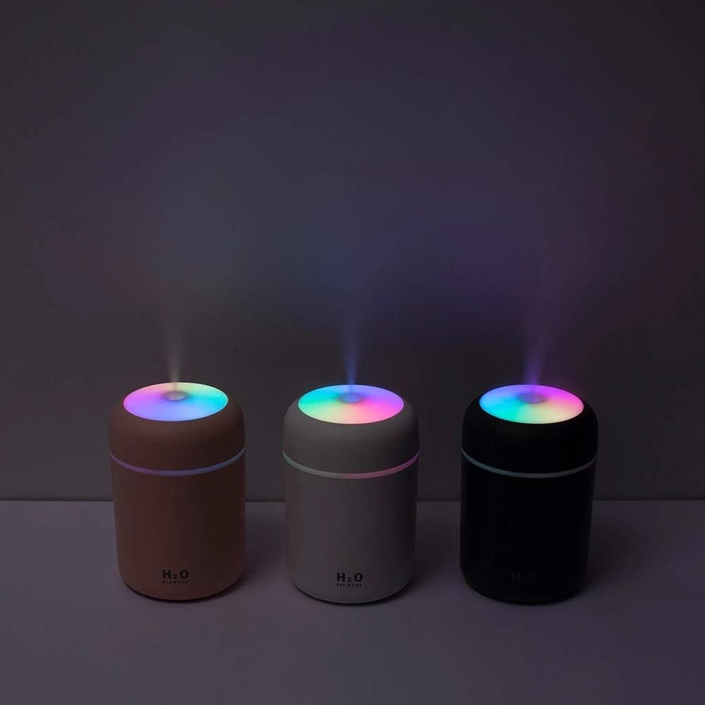 Drei zylindrische Luftbefeuchter, rosa, weiß und schwarz, die Dampf mit Regenbogenfarben abgeben. "H2O" ist auf zweien sichtbar.