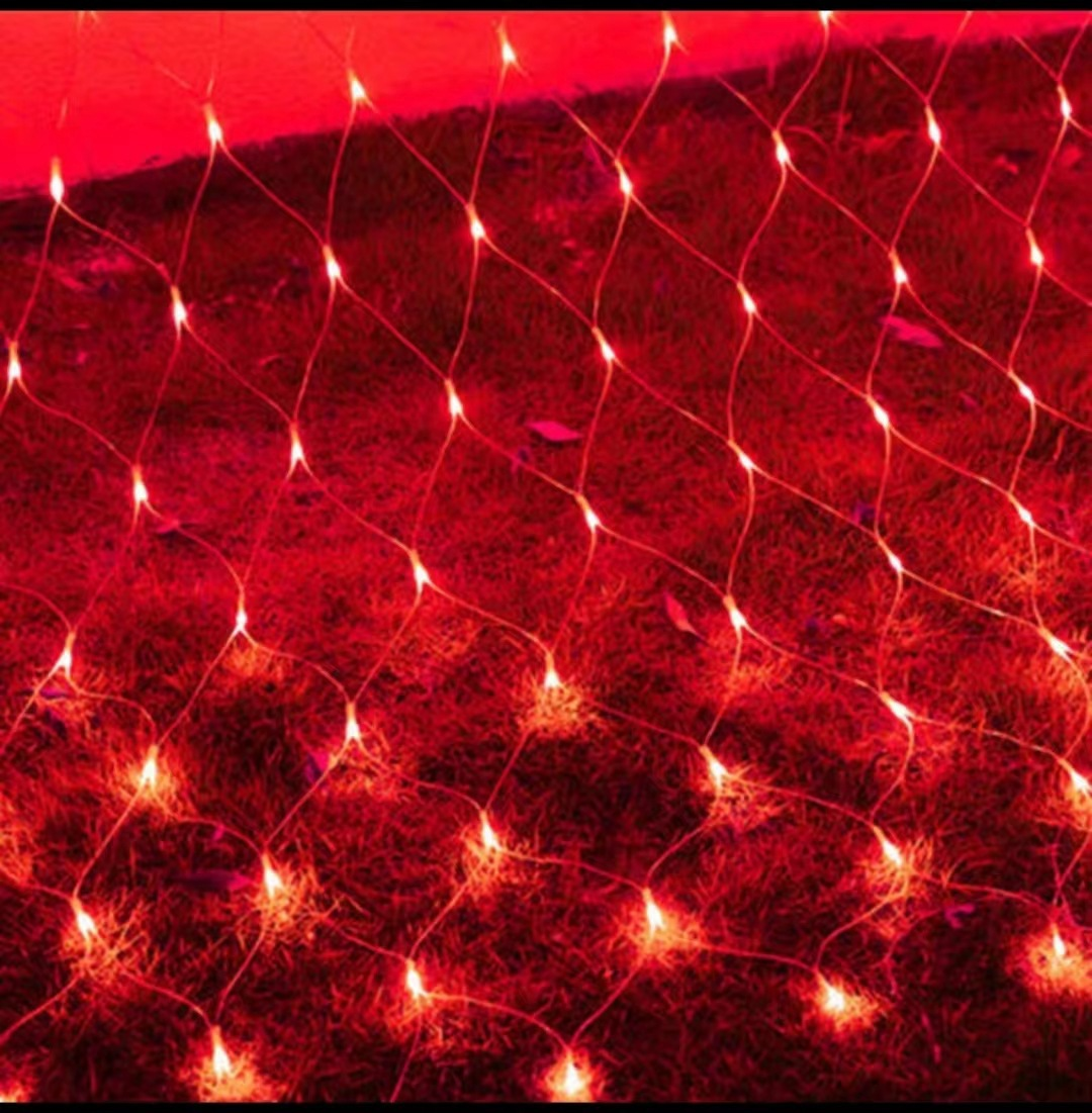 Rote Netzlichter auf Gras. Die Lichter sind an und erzeugen eine warme, festliche Atmosphäre. Das Gras erscheint dunkelrot.