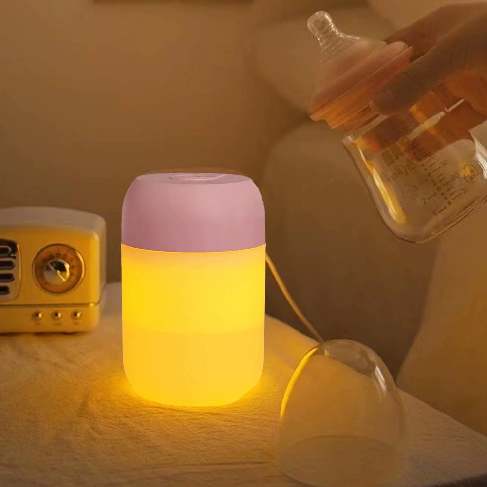 Ein Nachtlicht mit rosa Oberteil und gelbem Licht steht auf einem Tisch. Eine Person hält eine Babyflasche. Im Hintergrund steht ein gelbes Radio.
