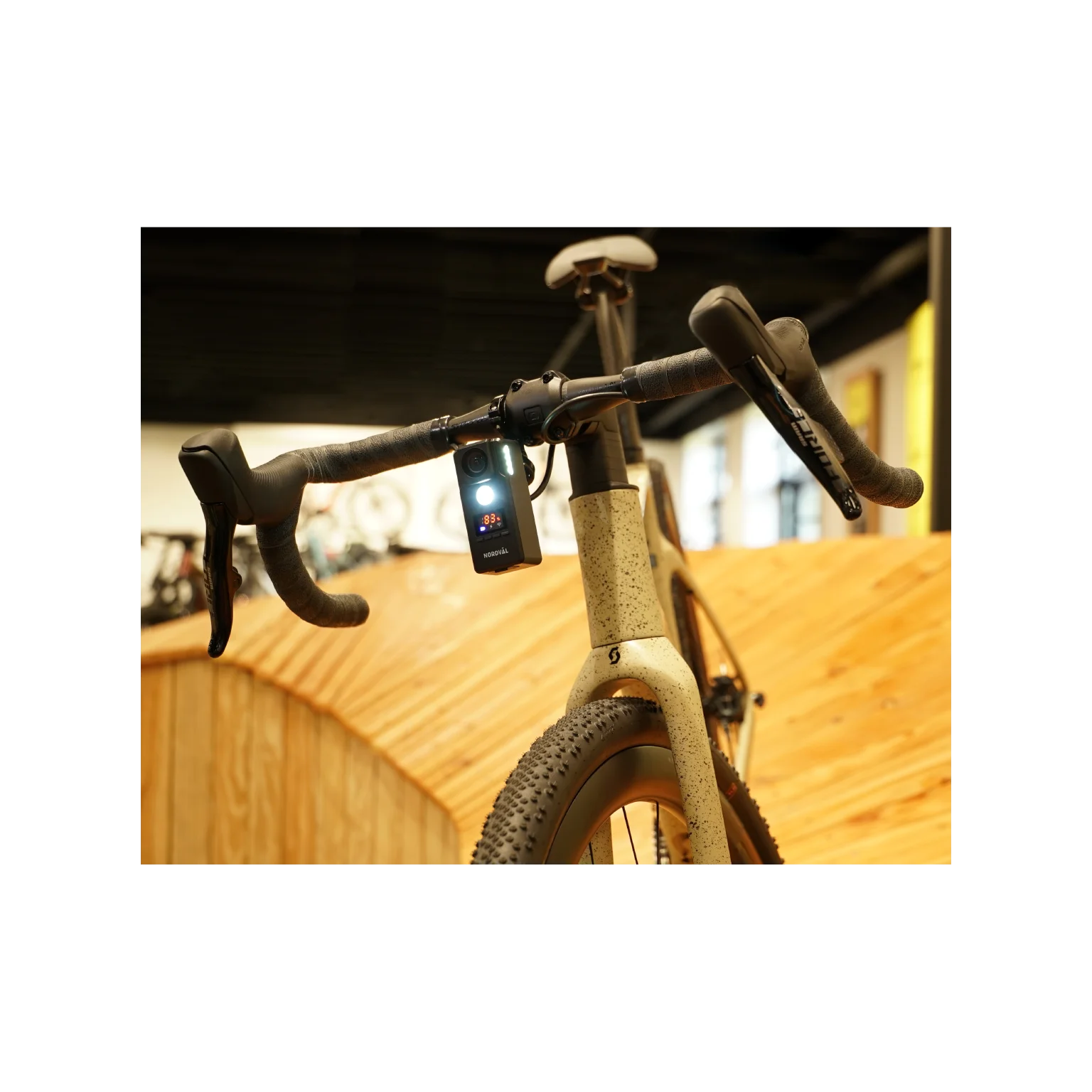 A bicycle with a light on the handlebars. The bike is light-colored with black handlebars. Wooden paneling is in the background.