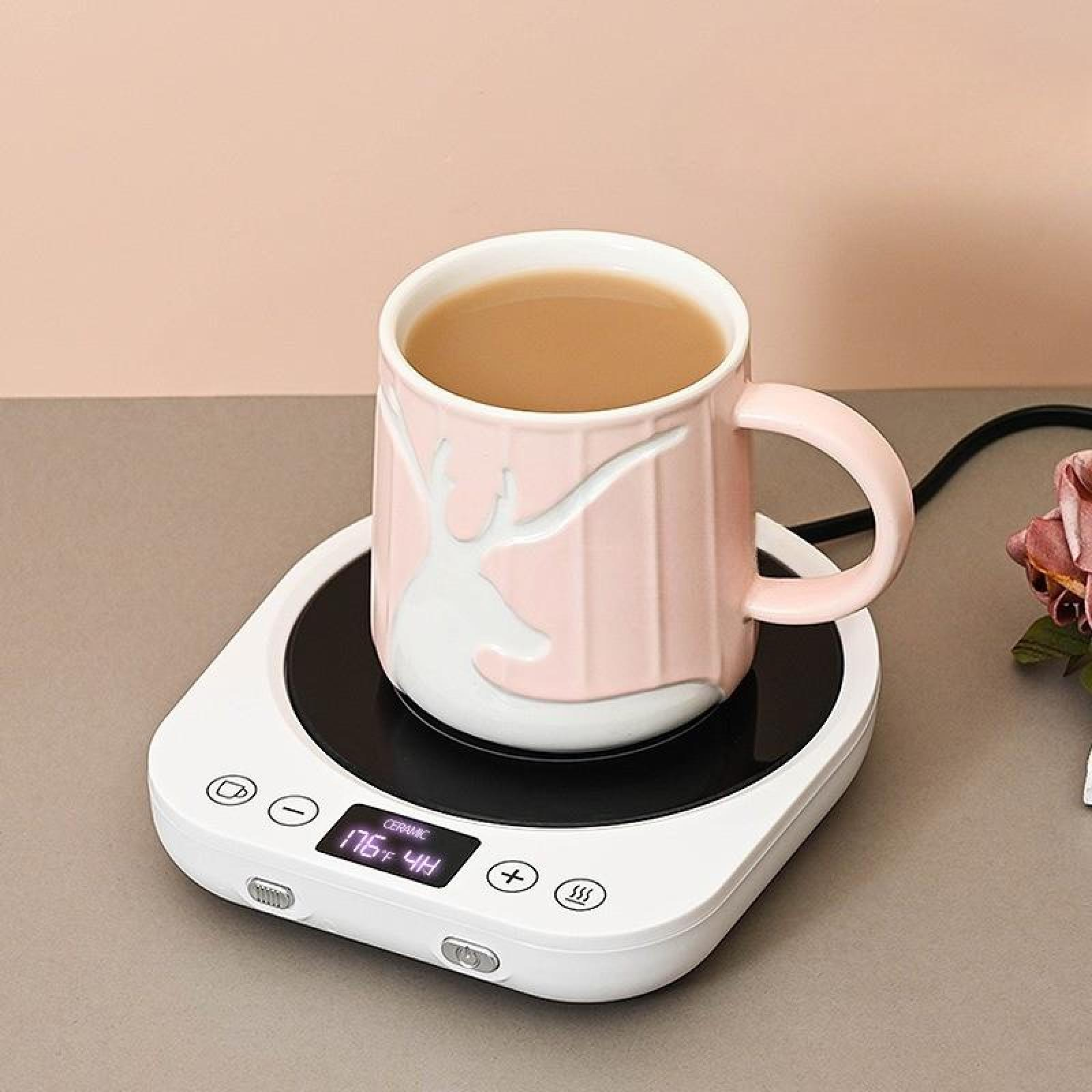 Eine rosa Tasse mit Hirschmotiv, gefüllt mit Tee, steht auf einem weißen elektrischen Tassenwärmer. Der Hintergrund ist hellrosa.