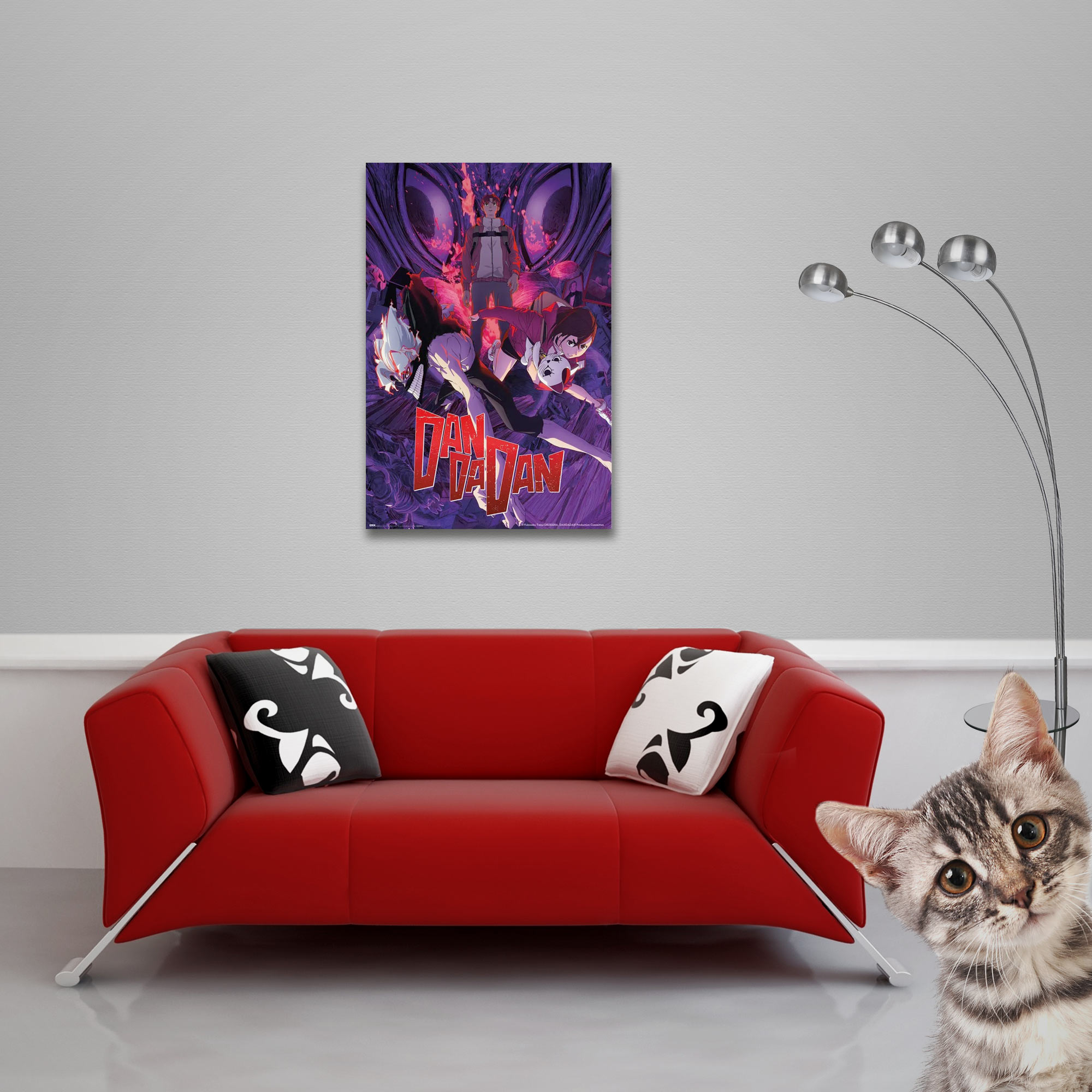 Rotes Sofa mit schwarz-weißen Kissen, Poster und Katze, die in die Kamera schaut. Rechts eine Stehlampe.