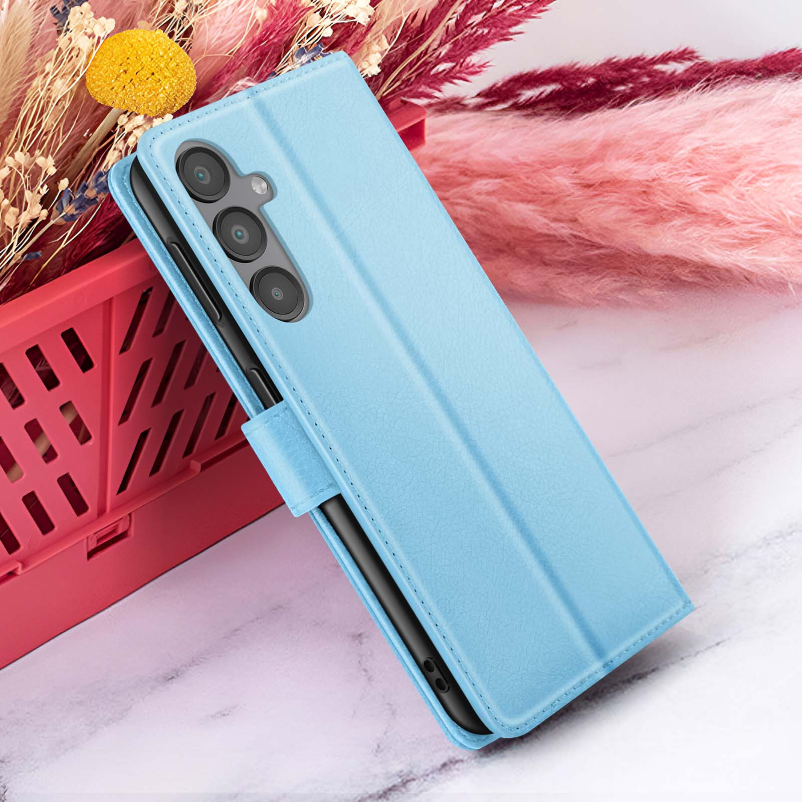Een blauwe telefoonhoes met een telefoon erin, geplaatst voor roze en rode bloemen.