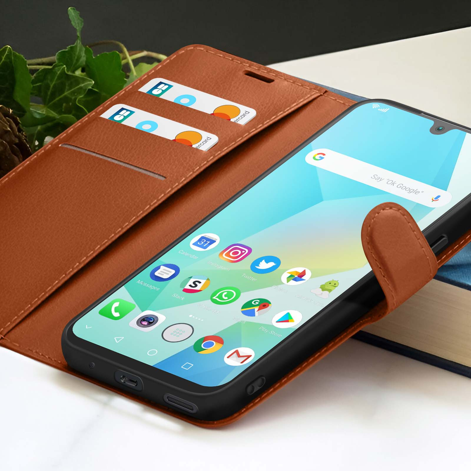 Een smartphone in een bruine leren hoes met creditcards en een boek op de achtergrond. De telefoon geeft app-iconen weer.