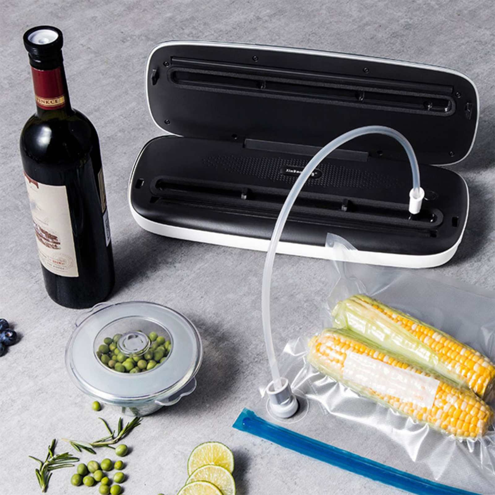Ein Vakuumierer mit Mais, Erbsen, Wein und Limetten. Lebensmittel befinden sich in einem Vakuumbeutel und einem Behälter. Die Maschine ist offen.