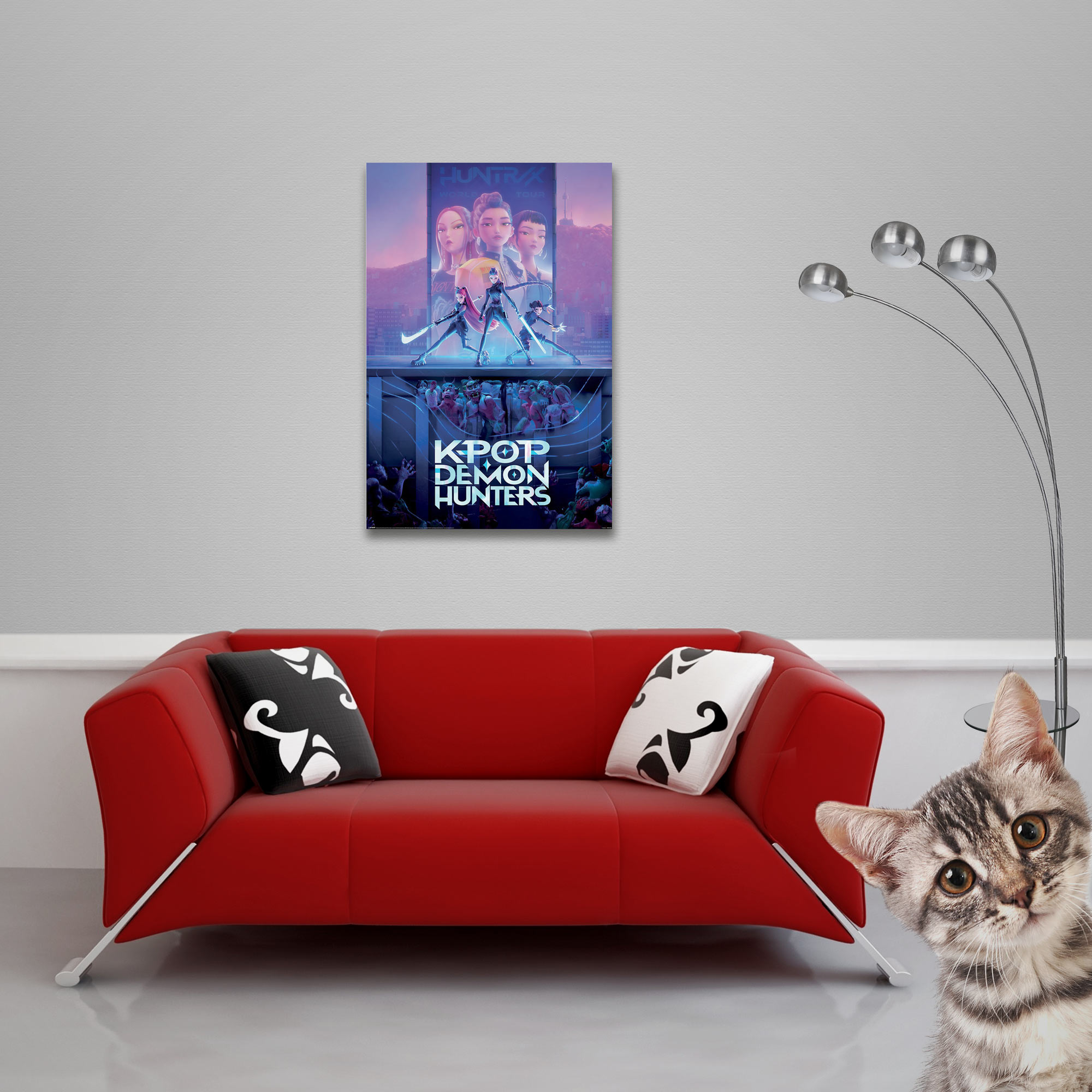 Ein rotes Sofa mit Kissen, ein Poster, eine Stehlampe und eine Katze, die in die Kamera schaut.