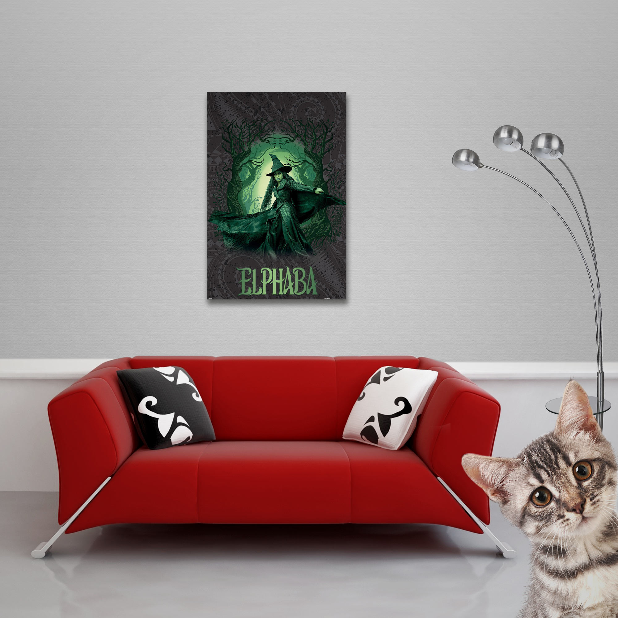 Rotes Sofa mit Kissen unter einem Poster von Elphaba. Eine Katze schaut von rechts. Eine Lampe steht im Hintergrund.
