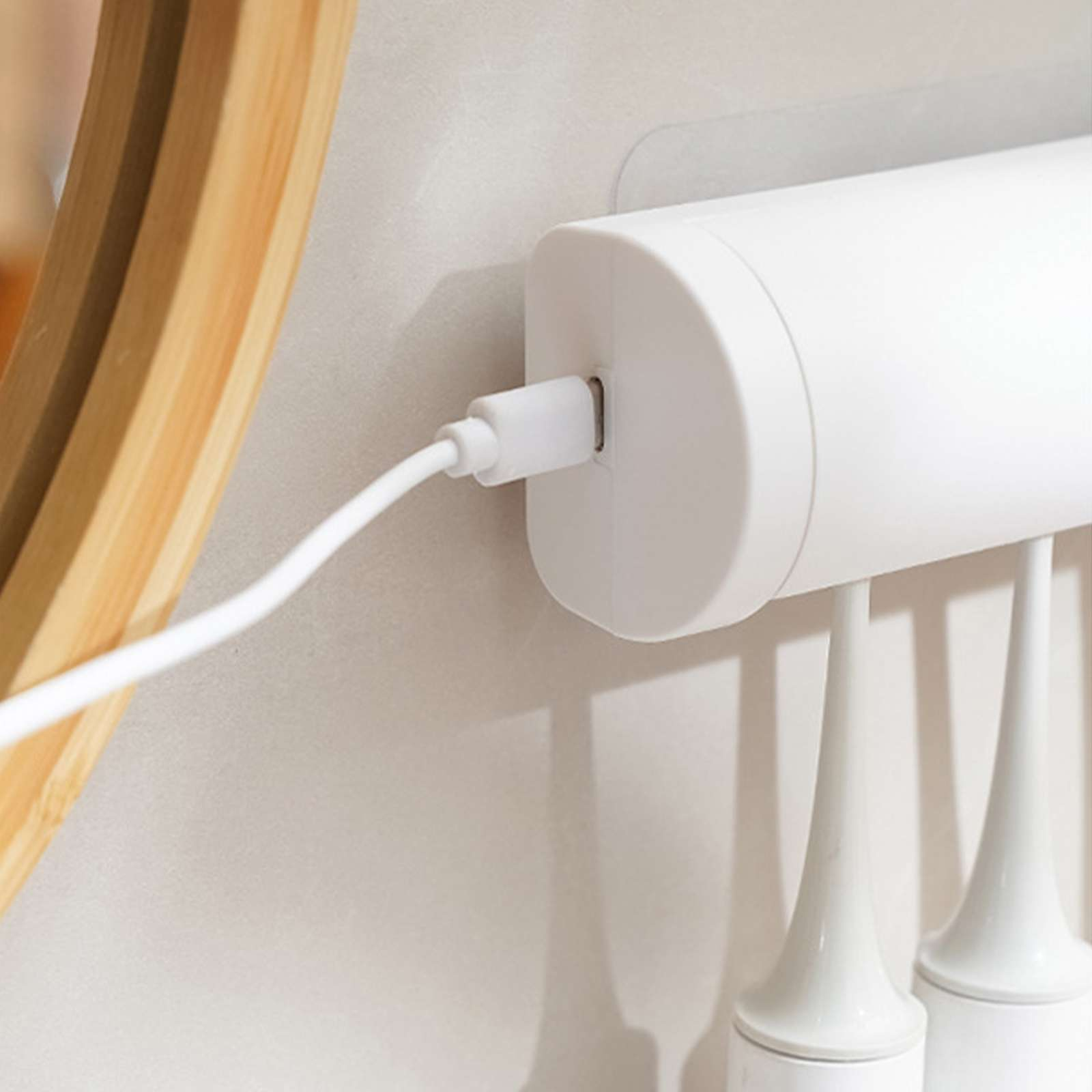 Ein weißes elektrisches Zahnbürstenladegerät, eingesteckt, an einer Wand hängend. Ein Holzspiegelrahmen ist teilweise sichtbar.