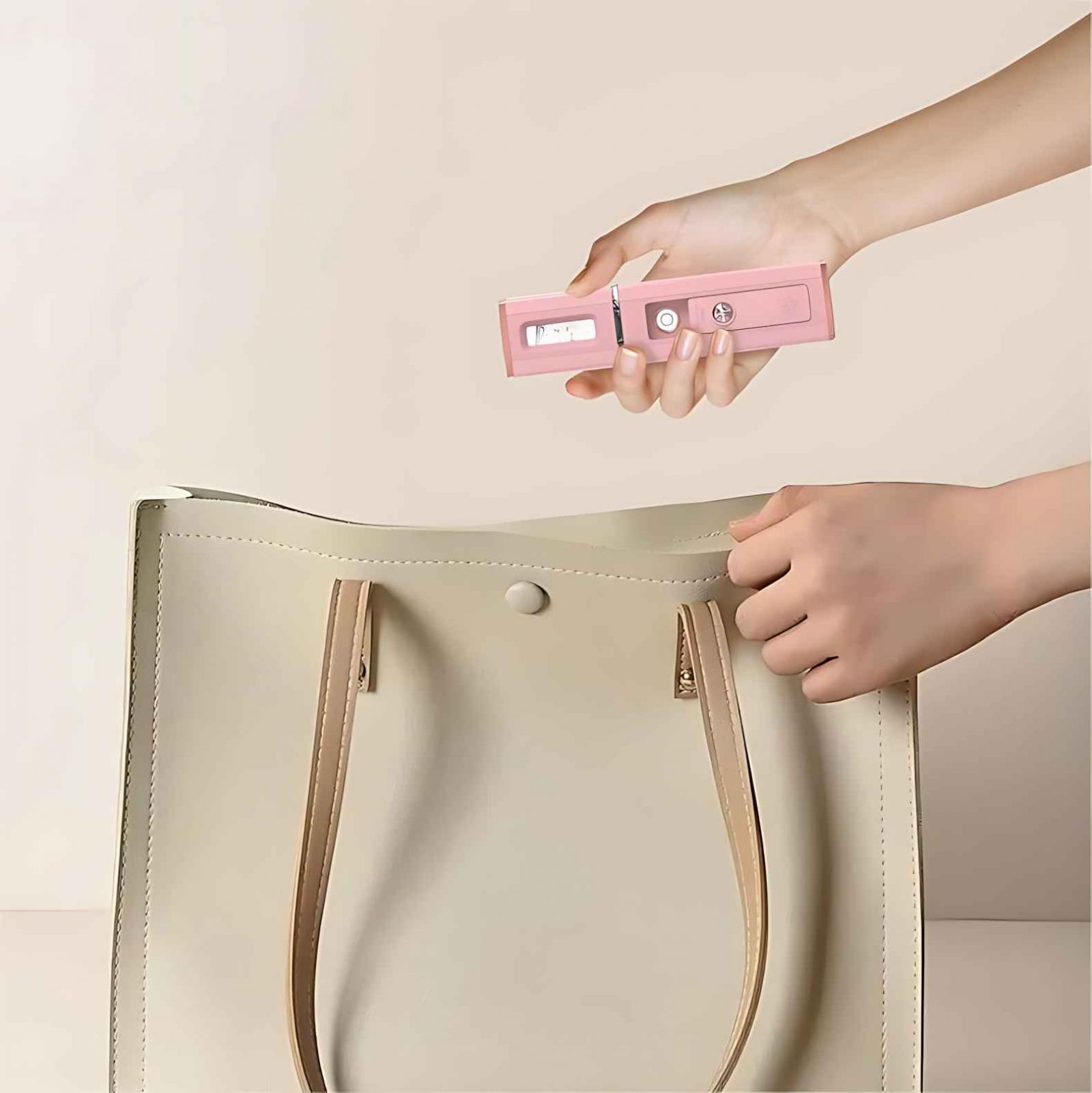 Hand hält pinkfarbenes Gerät über cremefarbener Tragetasche. Andere Hand in der Nähe der Tasche. Der Hintergrund ist hellrosa.