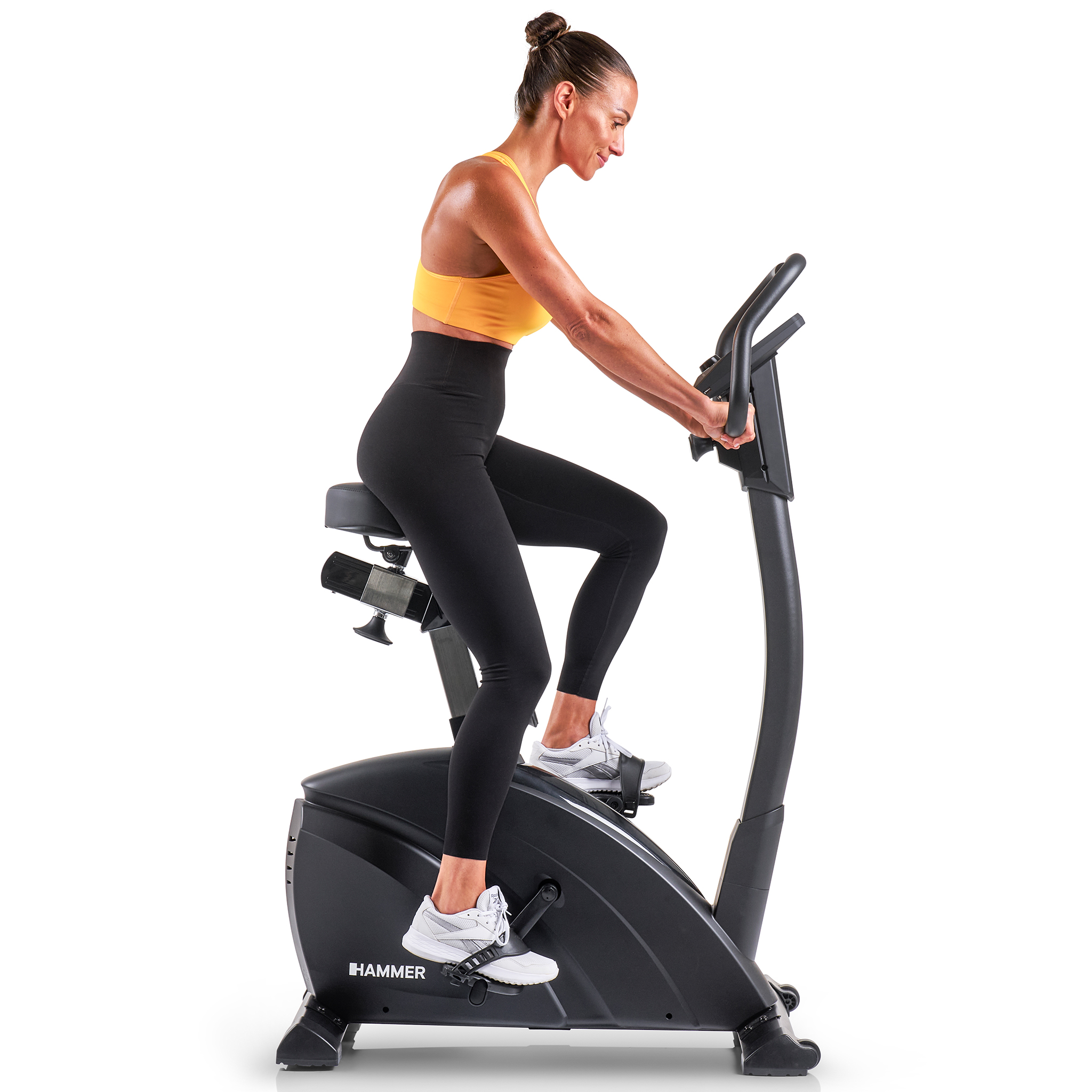 Eine Frau in Sportkleidung fährt auf einem Heimtrainer Fahrrad. Sie ist konzentriert und trainiert offensichtlich.
