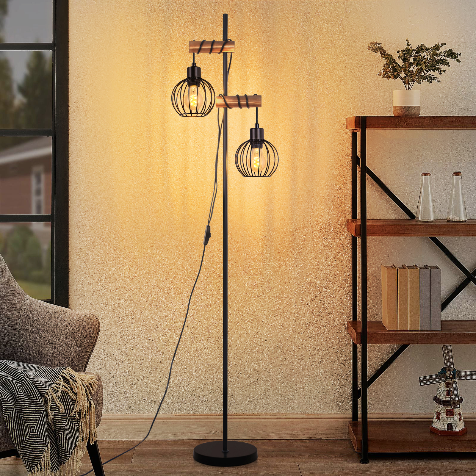 Una lampada da terra nera con due luci a gabbia. Una mensola in legno con libri, vasi e un mulino a vento. Una sedia grigia con una coperta.